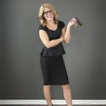 Blonde woman wearing black dress and black shoes posing wearing and holding black plastic frames. Blonde female wearing turquoise plastic designer frame Maple Grove Eye Doctors at Pearle Vision
