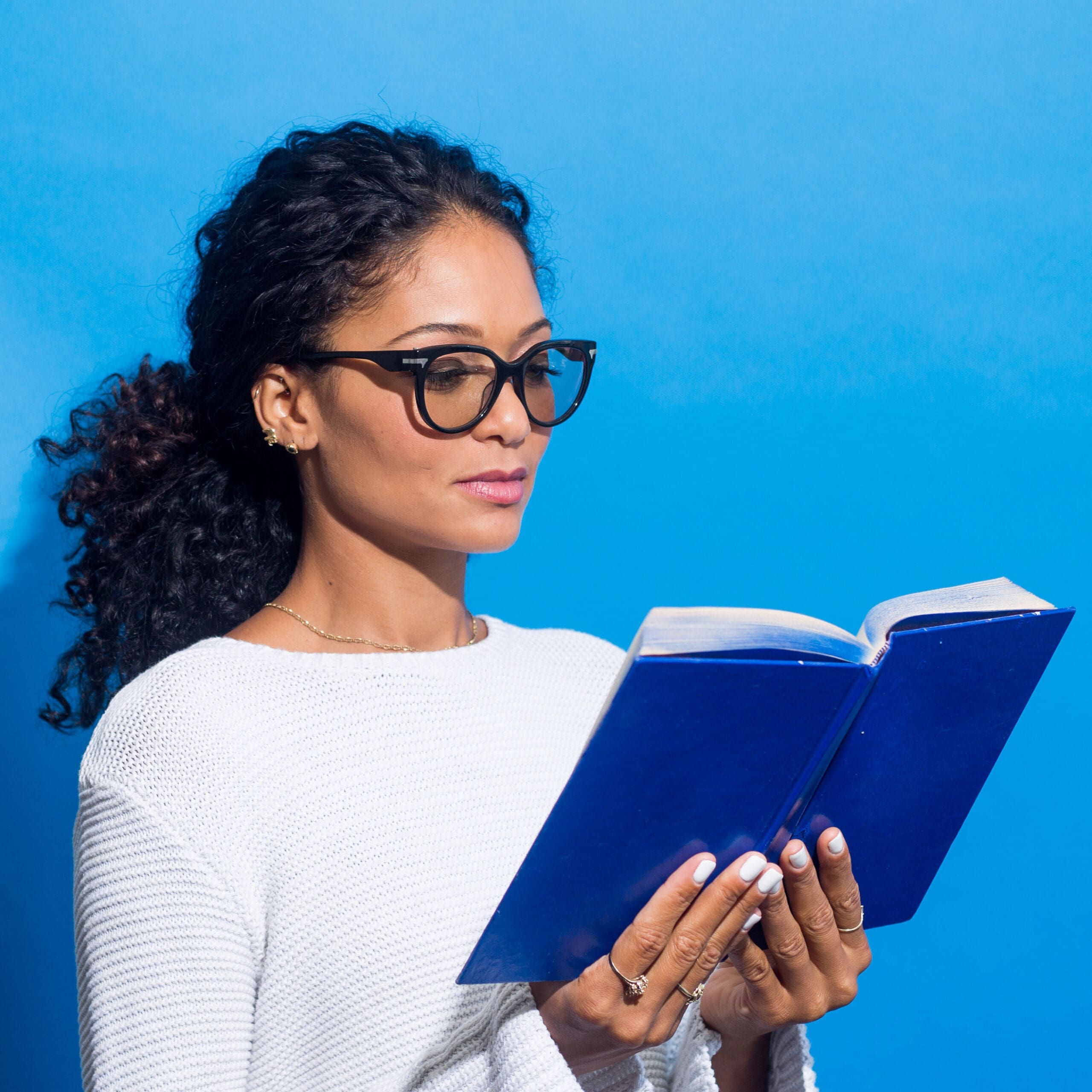 African American woman with long black hair holding book and wearing black round plastic frame with Transitions lenses Maple Grove Eye Doctors at Pearle Vision