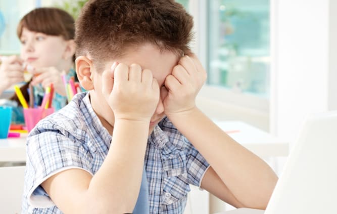 brown haired young Boy sitting in front of laptop rubbing his eyes Maple Grove Eye Doctors at Pearle Vision