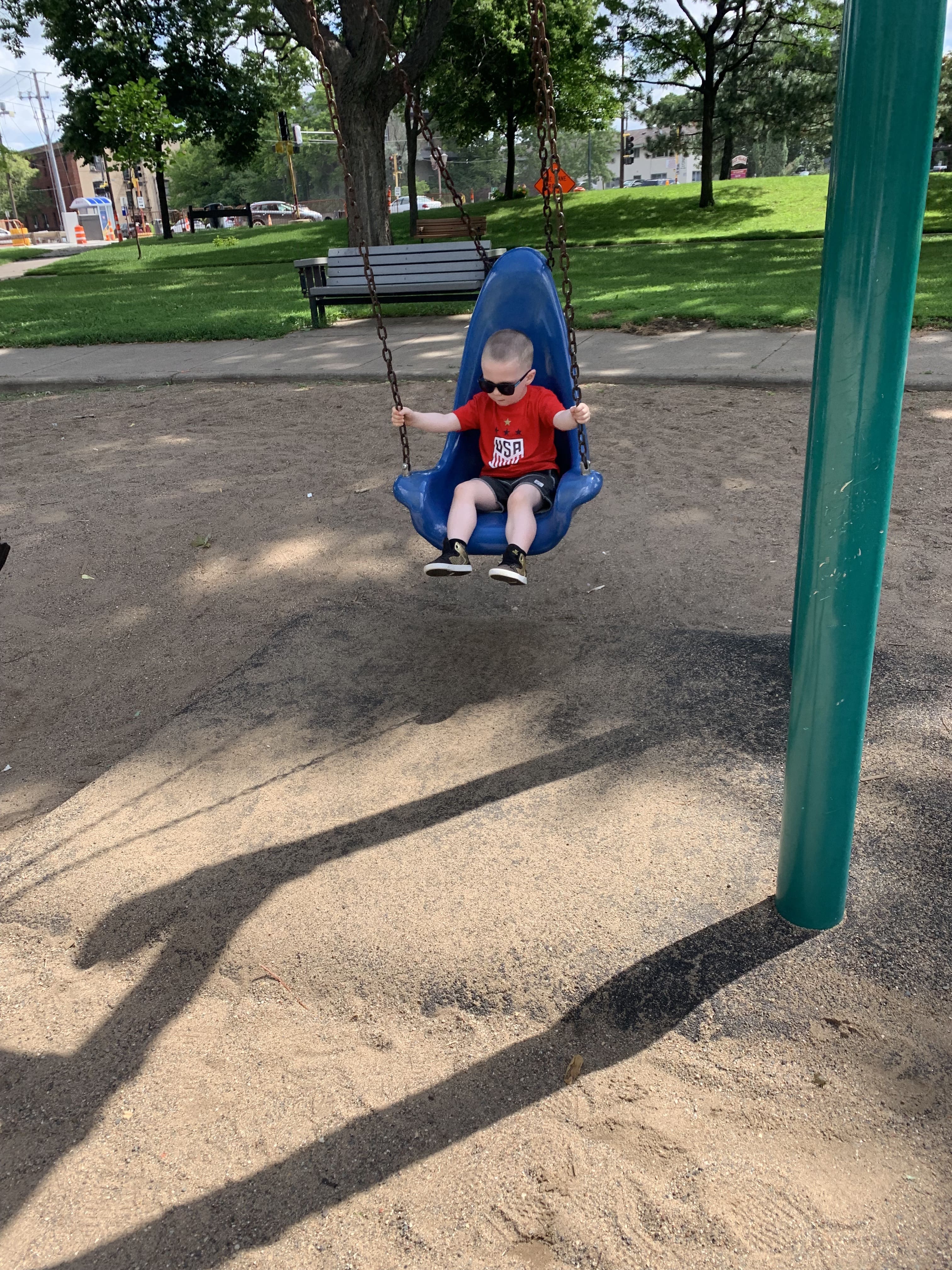 Toddler boy on swing wearing sunglasses . Maple Grove Eye Dcotors