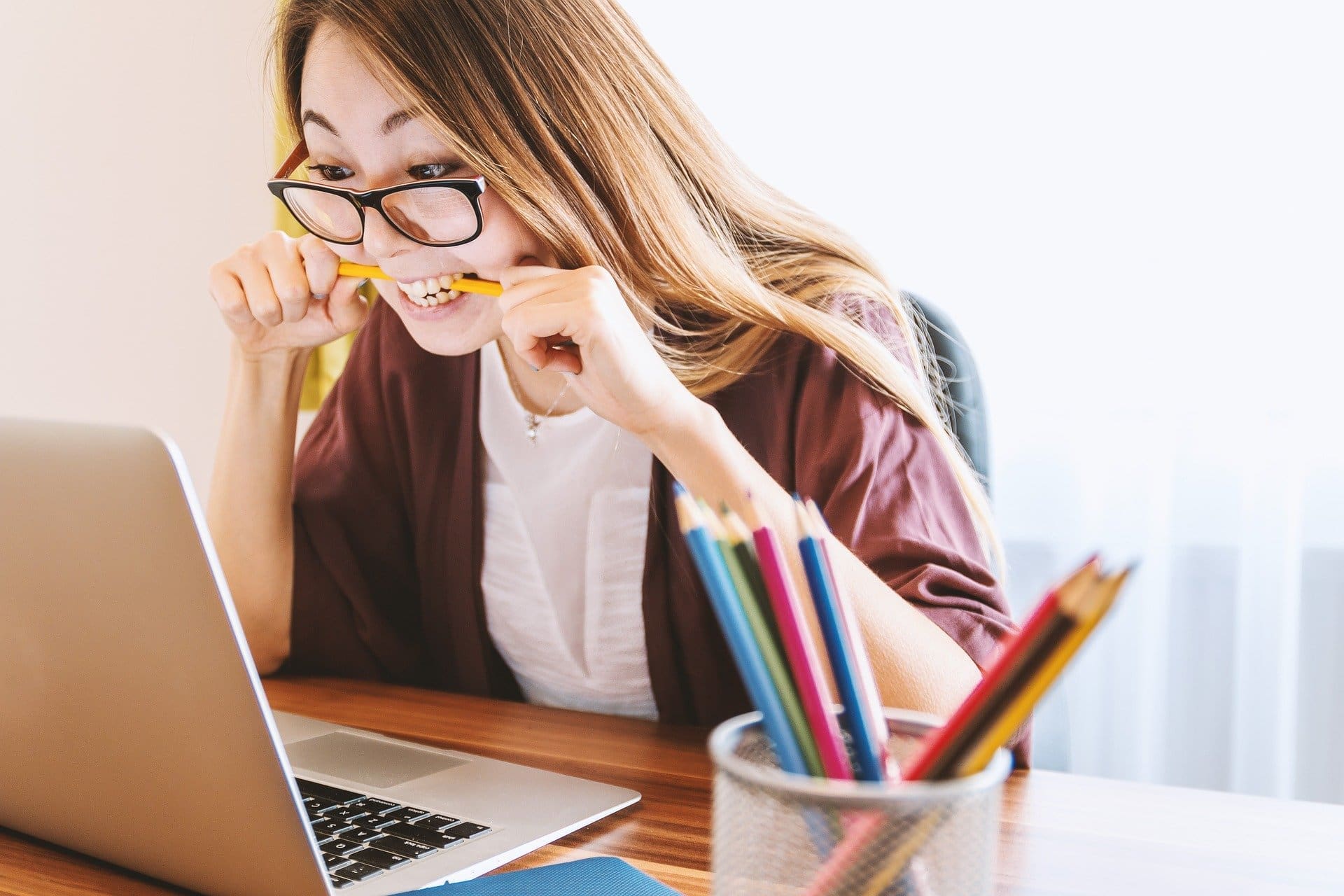 Girl with brown hair sitting in front of a laptop wearing yellow and black glasses while biting on pencil Maple Grove Eye Doctors at Pearle Vision